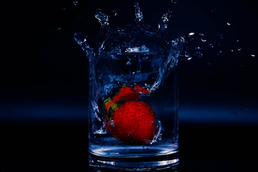 Ripe strawberry plunges into water creating a dramatic splash with frozen droplets against a dark backdrop.