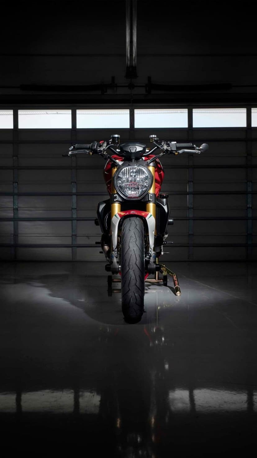 Red Ducati motorcycle parked in a dark garage with a clear reflection on the polished floor and golden accents.