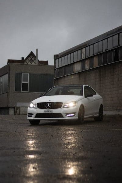 White Mercedes Coupe on Rainy Urban Street Phone Wallpaper