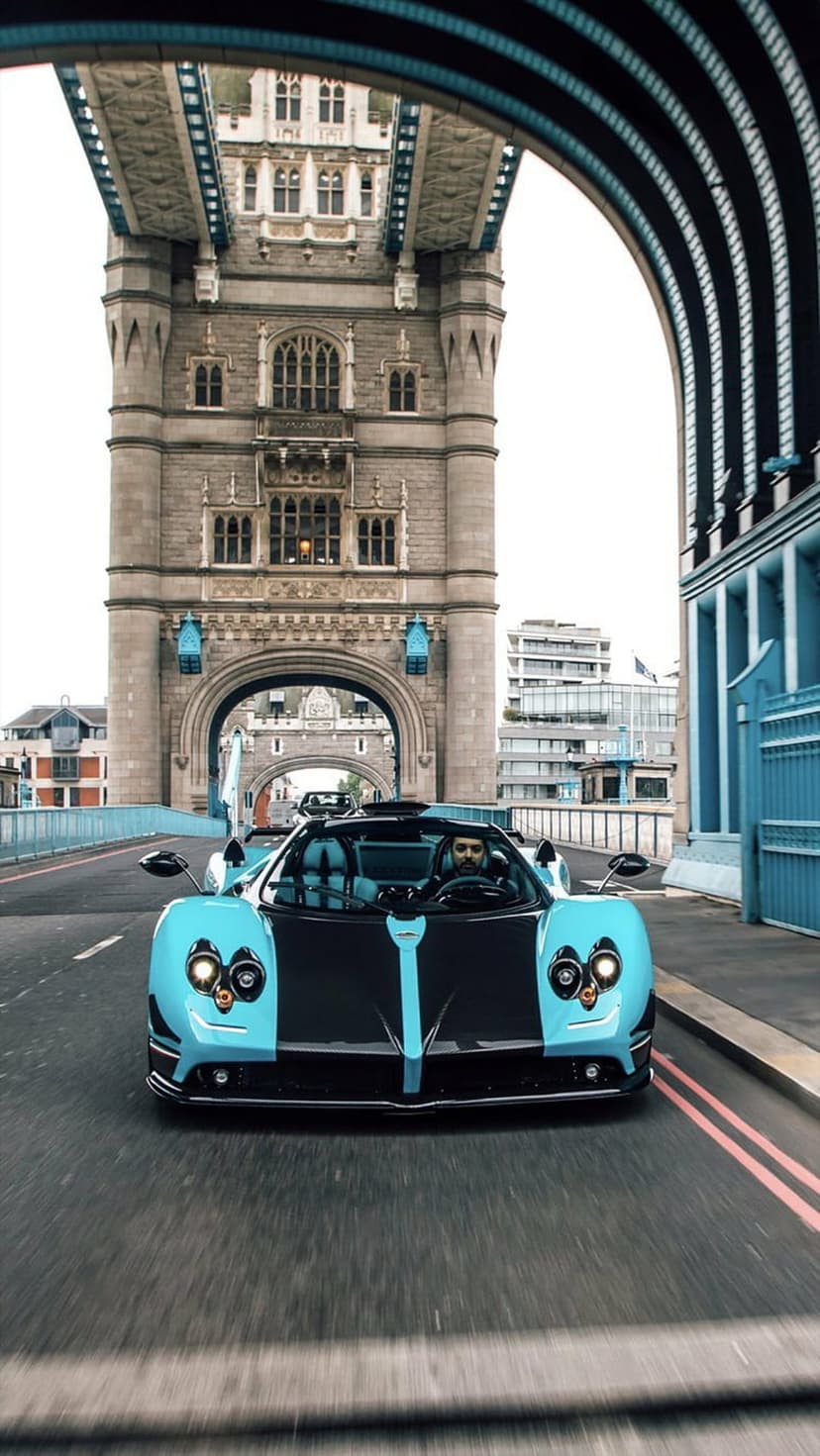Teal Pagani hypercar cruises over Tower Bridge asphalt showing the blue suspension cables and London architecture.