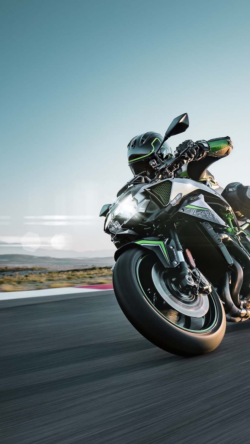 Green and black sportbike leaning into a racetrack turn with motion blur and a clear blue sky background.