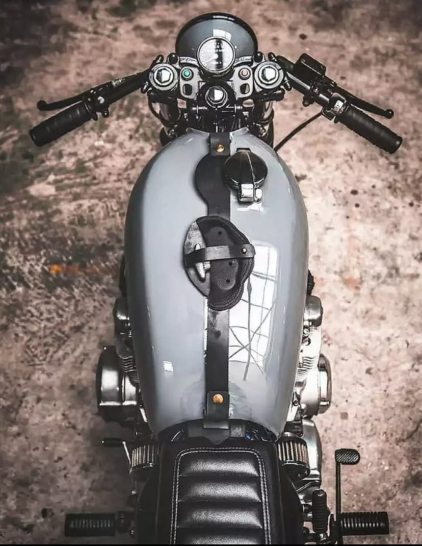 Custom cafe racer motorcycle fuel tank and clip-on handlebars viewed from above on a textured concrete surface.