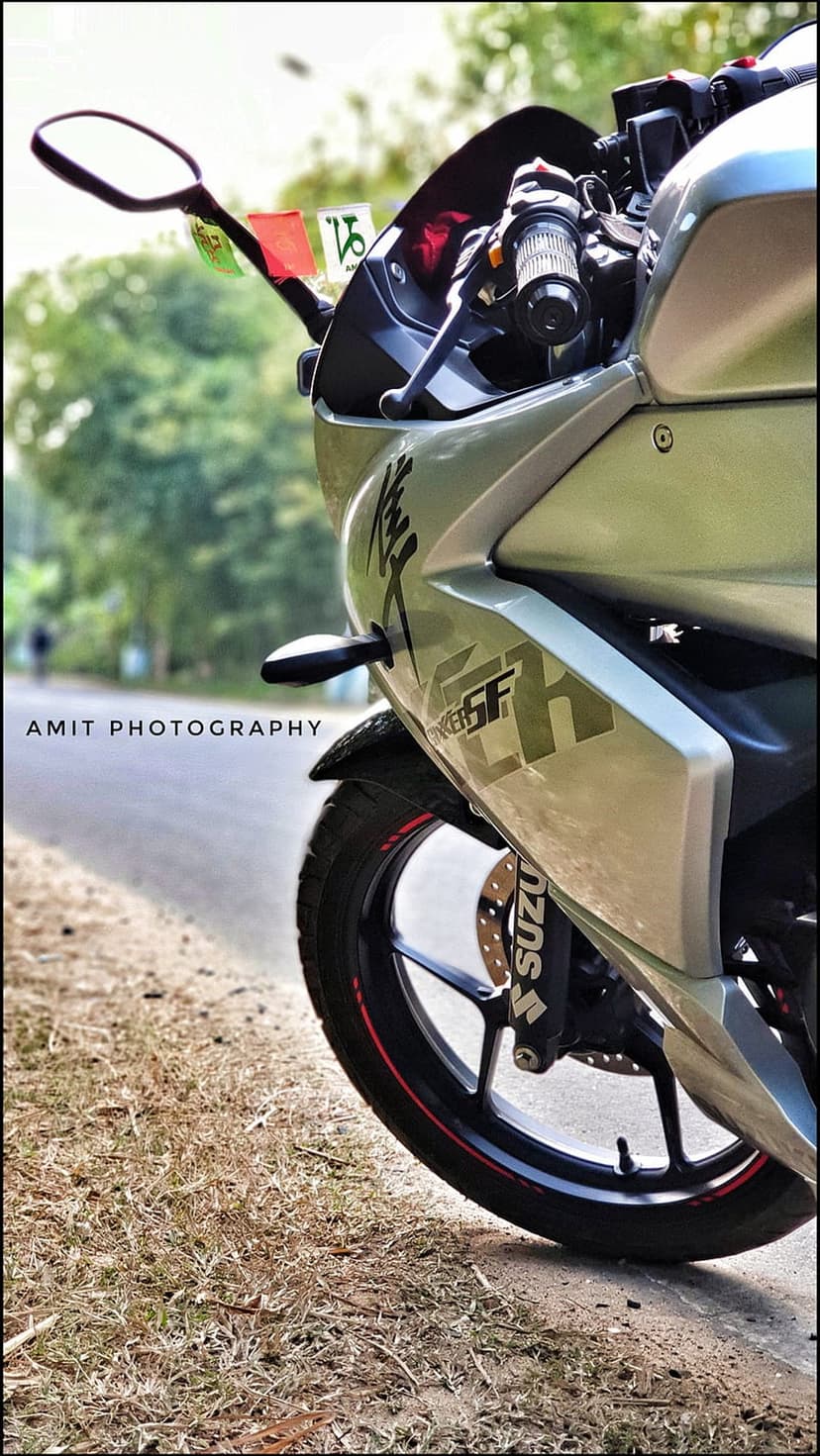 Silver Suzuki motorcycle fairing and front wheel parked on a grassy roadside with soft bokeh background.
