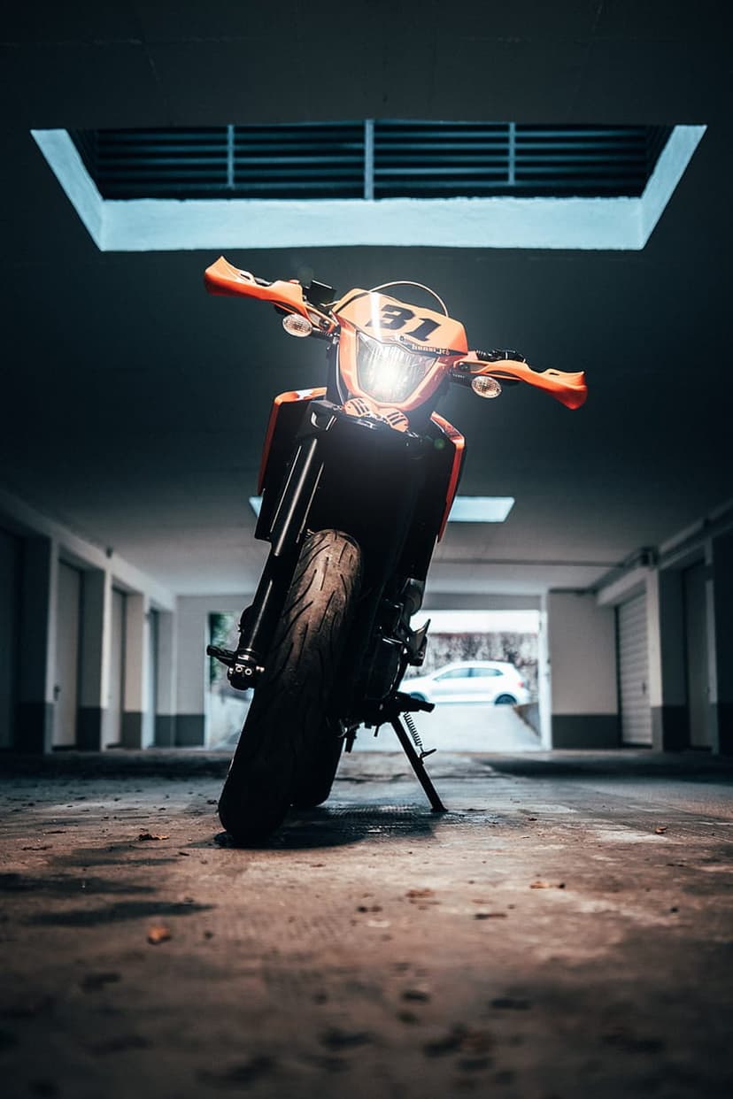 Orange supermoto motorcycle with number 31 plate parked on concrete in a dimly lit underground parking garage.