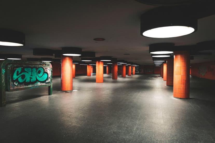 Orange pillars and green graffiti fill a deep perspective view of a modern underground subway station.