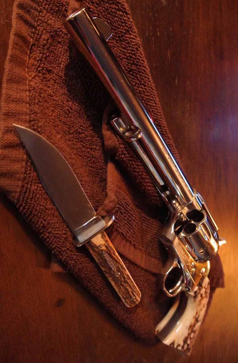 Chrome revolver and stag handle hunting knife laying on textured brown cloth over a rustic wooden surface.