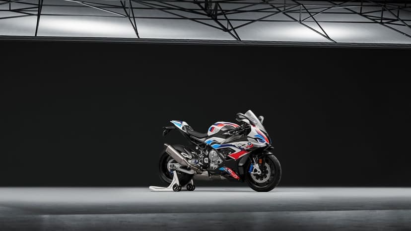 BMW M1000RR sport motorcycle with white, blue, and red livery on a racing stand in a minimalist dark studio.