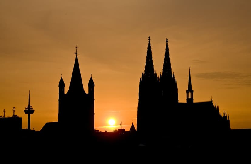Cologne Cathedral twin spires form a dark silhouette against a vibrant orange and yellow sunset sky in Germany.