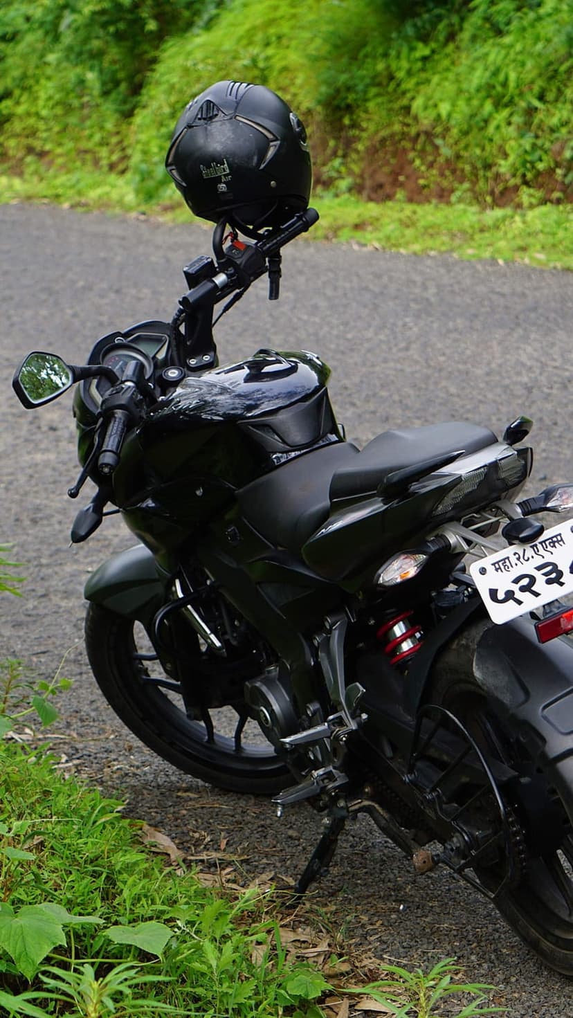 Black sport bike with a matching helmet sits on a gravel path bordered by dense green bushes and forest leaves.