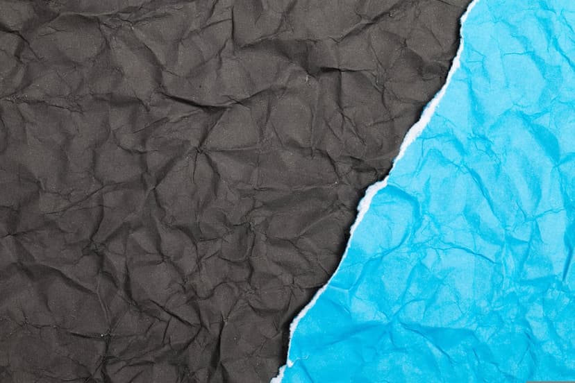 Crumpled blue and black paper with torn edges and sharp creases shows deep shadows and tactile surface textures.
