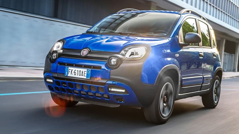 Blue Fiat Panda Cross driving on an urban road with modern buildings and a blurred motion effect.
