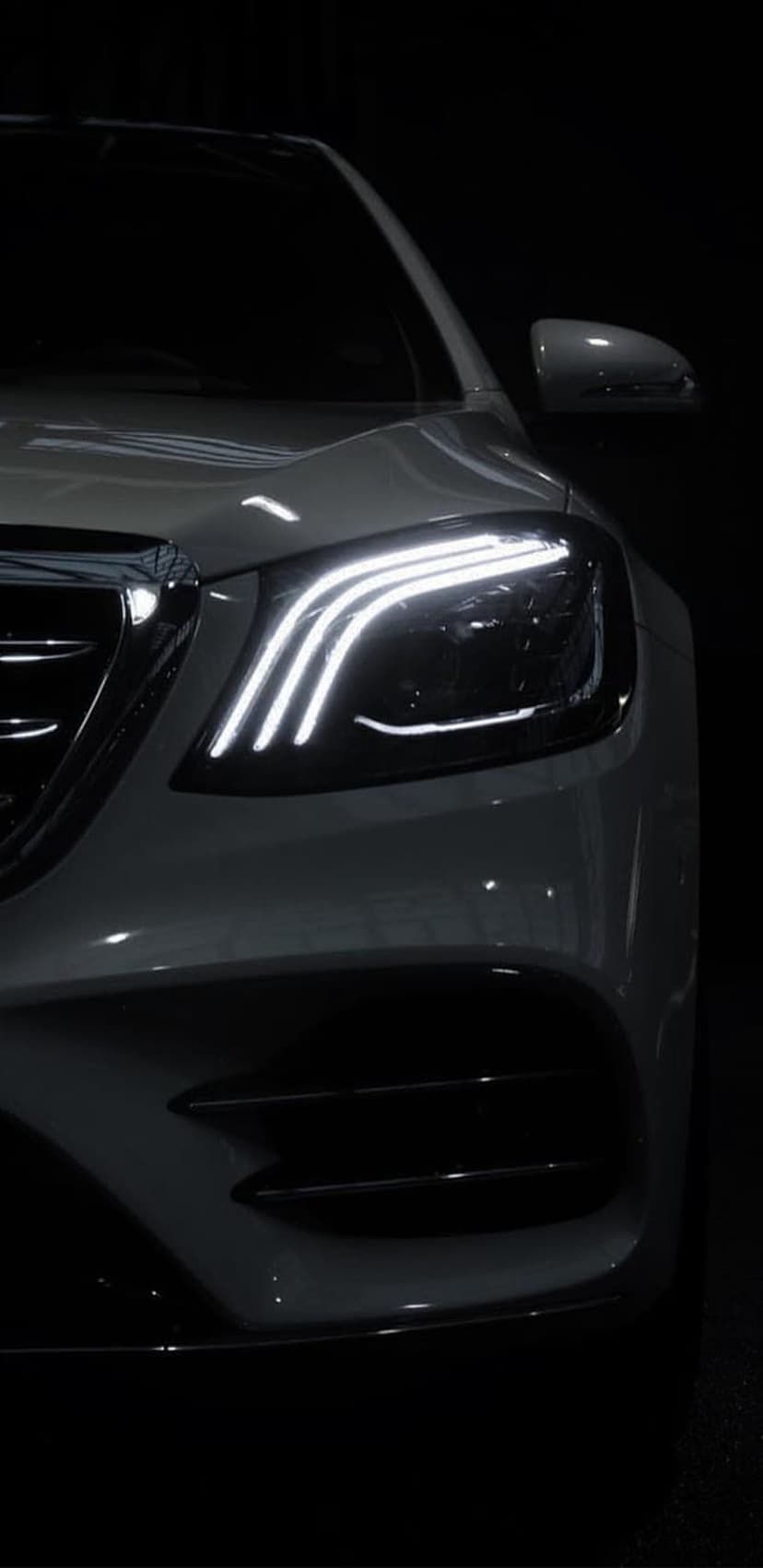 White luxury car headlight with glowing LED daytime running lights against a dark, minimalist background.