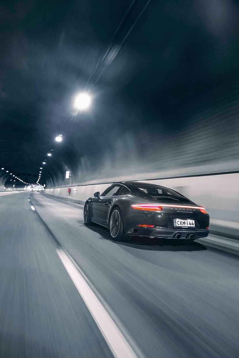 Porsche 911 sports car with red taillights racing through a concrete tunnel with motion blur on a wet road.