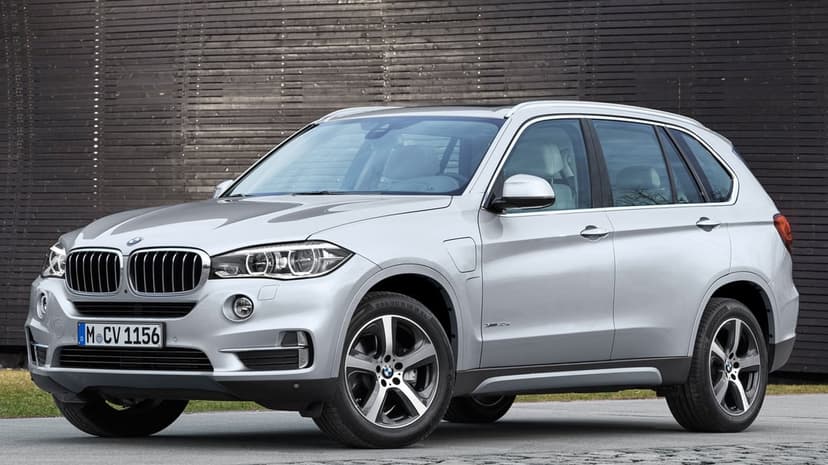 Silver BMW X5 luxury SUV with alloy wheels parked in front of a dark brown slatted wooden wall in daylight.