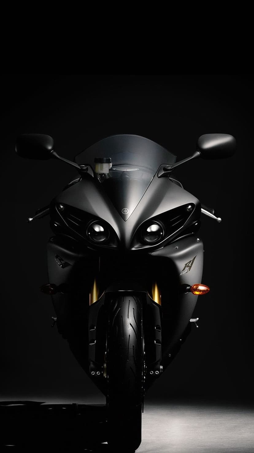 Front view of a matte black Yamaha R1 motorcycle with dual headlights and gold forks on a black background.