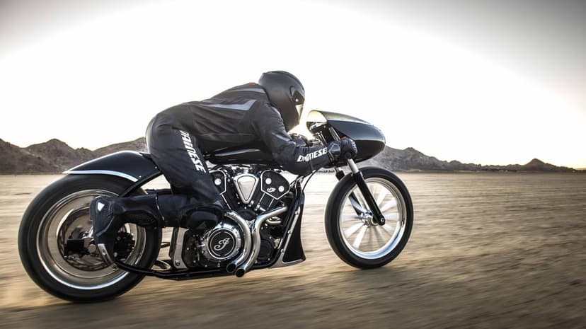 Motorcyclist in black leathers riding a custom chrome motorcycle at high speed across a desert dry lake bed.