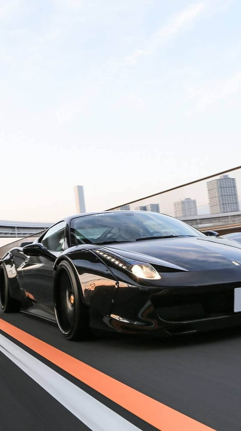 Ferrari 458 Italia supercar speeds down a dark urban road with illuminated headlights and visible motion blur.