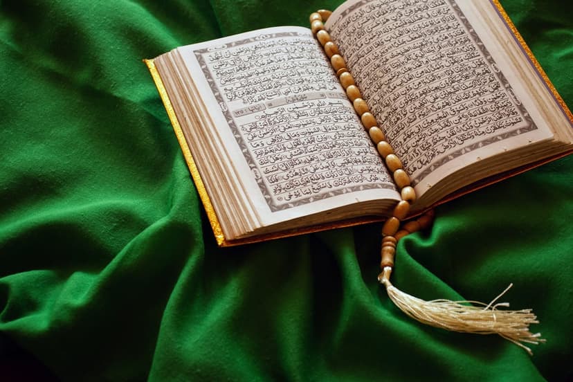 Open Holy Quran with Arabic script and wooden prayer beads resting on textured green cloth in soft light.