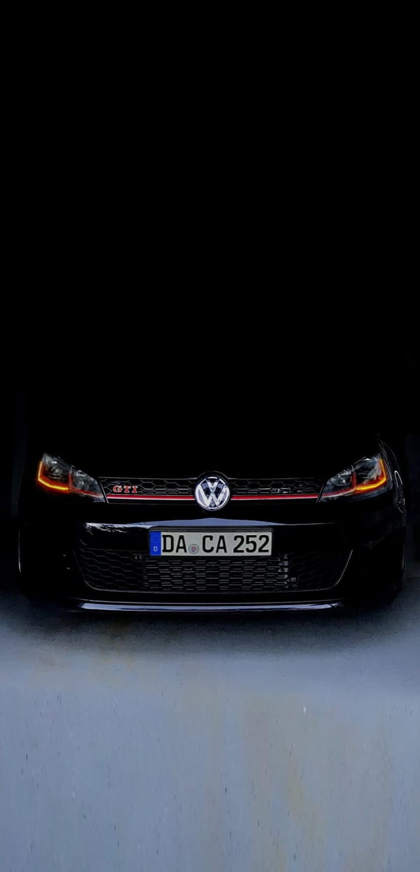 Black Volkswagen Golf GTI with glowing orange headlights and a red grille stripe in a dark parking garage.