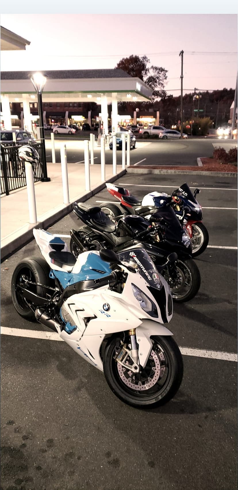 BMW S1000RR and sport motorcycles parked at a lit gas station at night, featuring sharp fairings and neon glow.