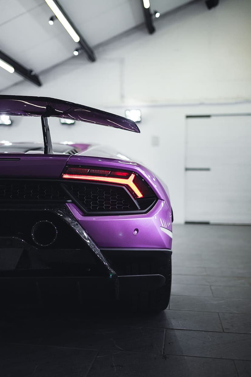 Purple Lamborghini rear with glowing Y-shaped LED lights, a large aerodynamic spoiler, and dual exhaust pipes.