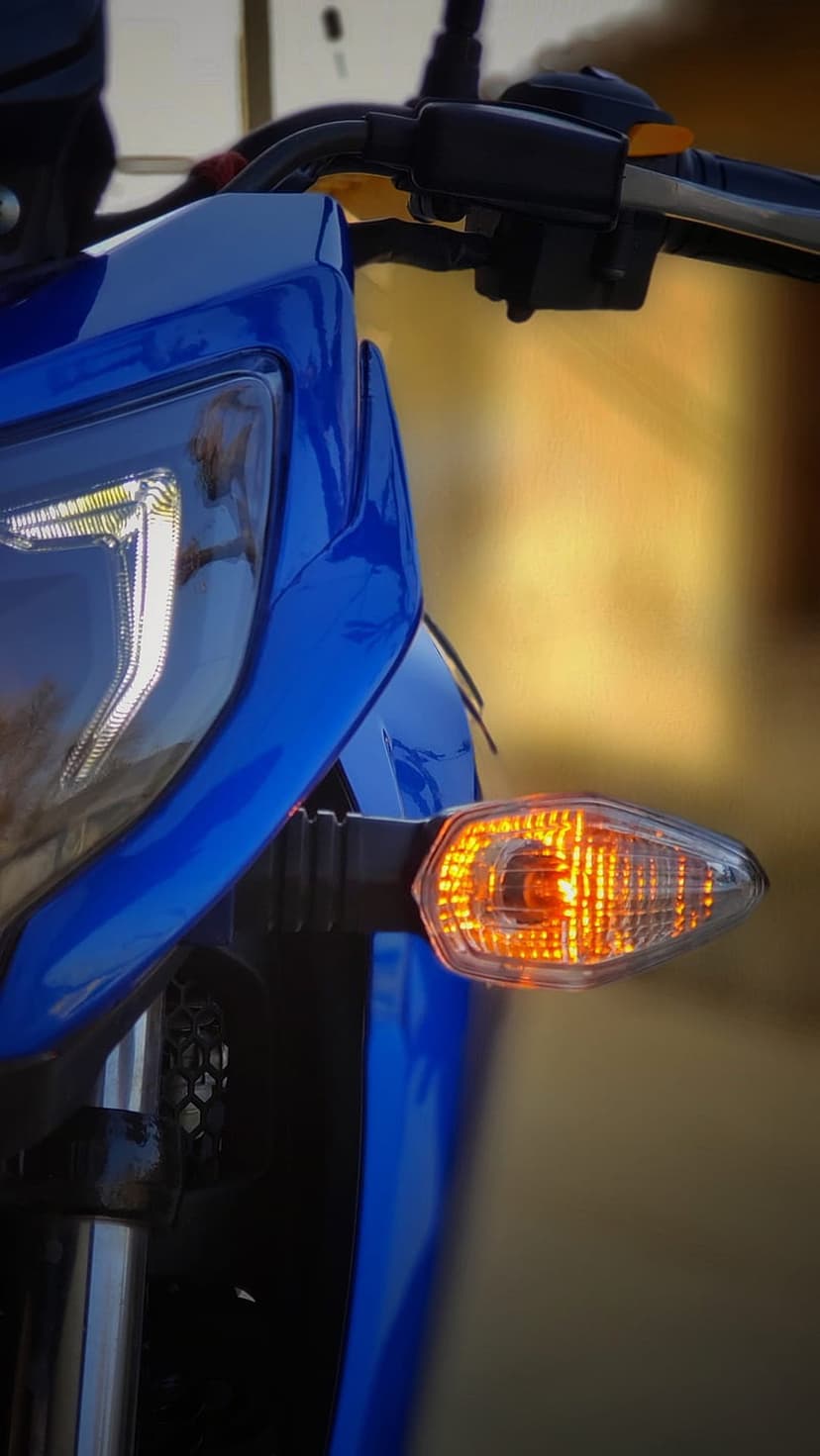 Blue motorcycle headlight and amber turn signal glow against polished metallic forks and cerulean paint.