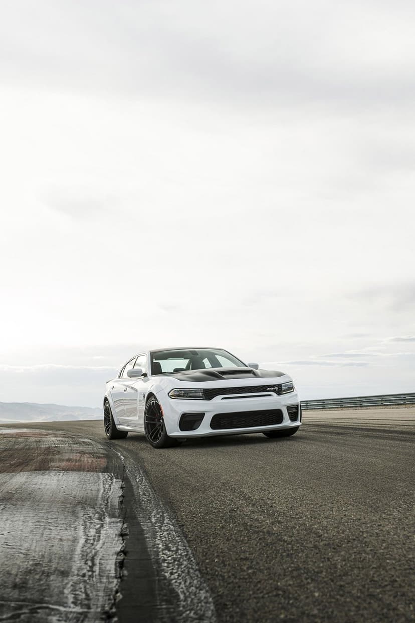 White Dodge Charger SRT Hellcat Widebody with a black hood on a racetrack under a bright overcast morning sky.