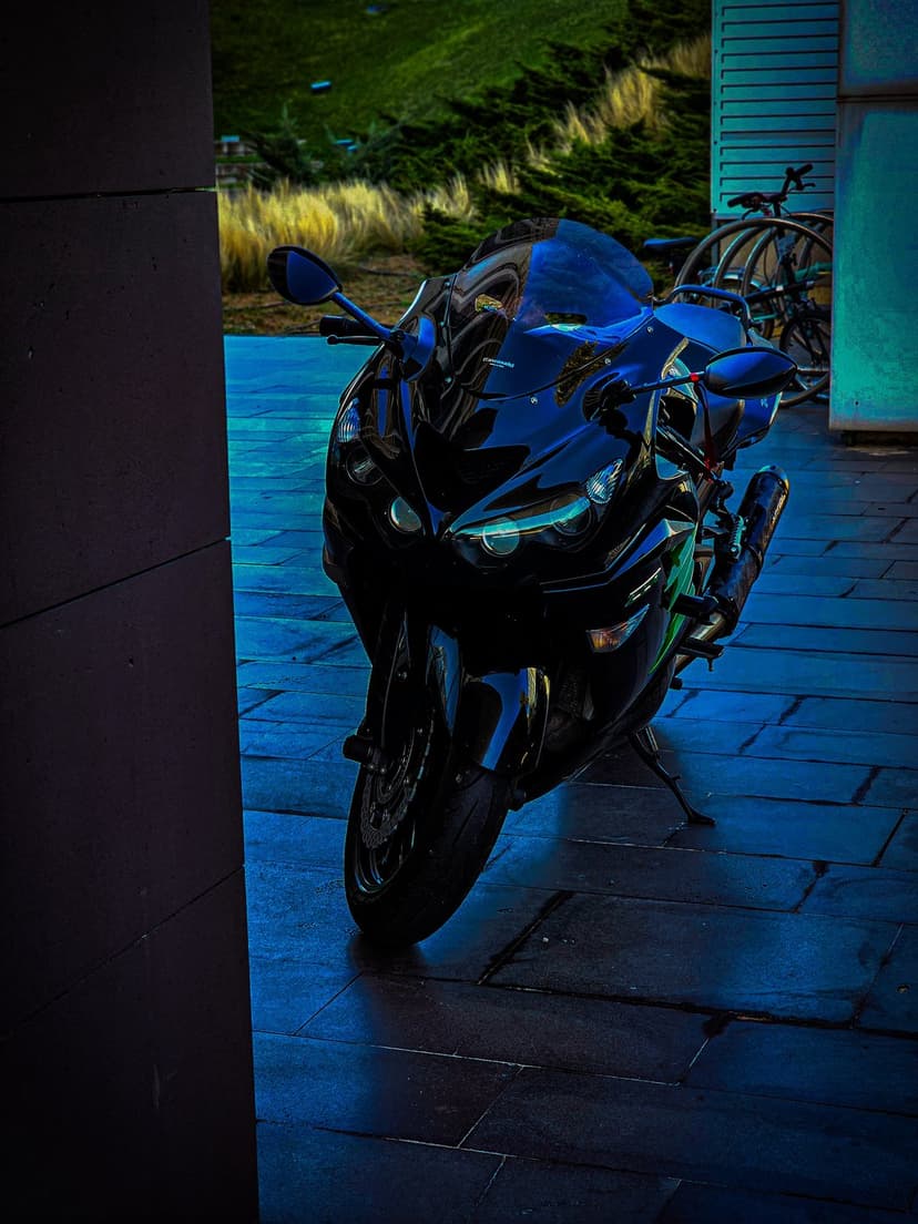 Black sport motorcycle parked on blue geometric tiles with a blurred green hill and bicycle in the background.