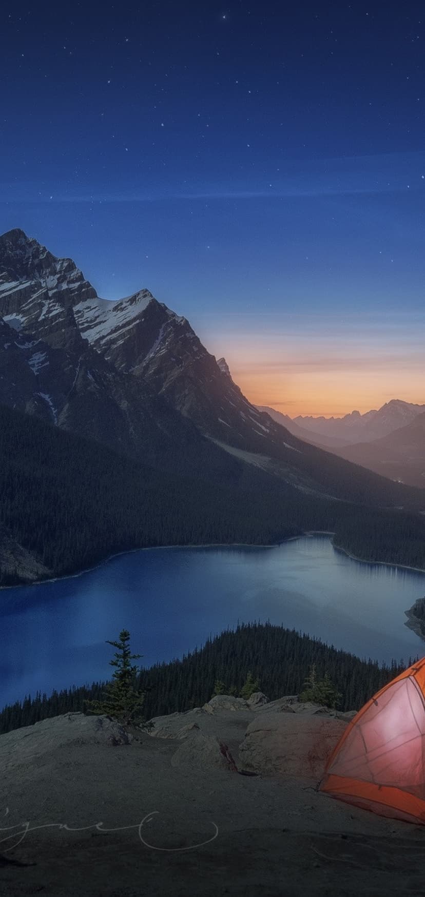 Glowing orange tent on a rocky cliff overlooking a blue lake and snow-covered mountains under a starry sky.