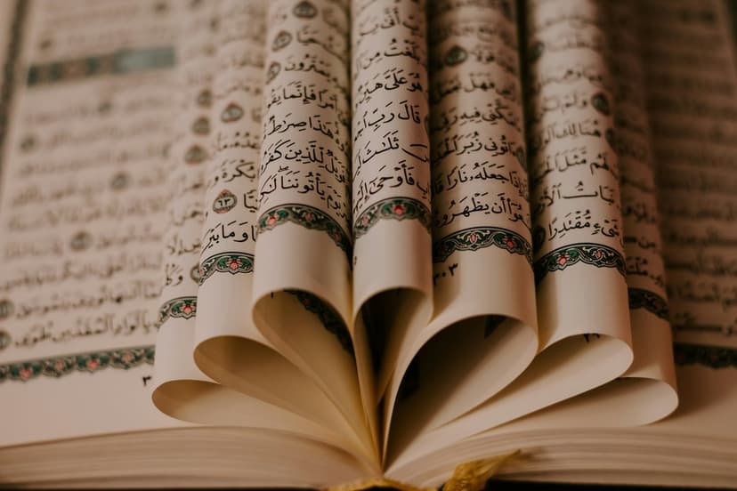 Folded Quran pages forming a heart shape highlight elegant Arabic calligraphy under warm and soft glowing light.