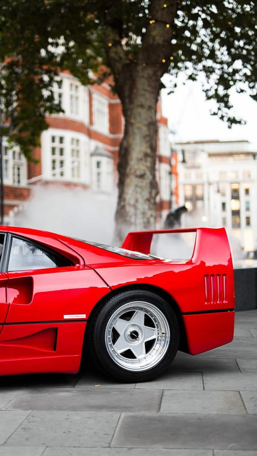 Red Ferrari F40 side profile on cobblestones with festive lights and brick buildings in the blurry background.