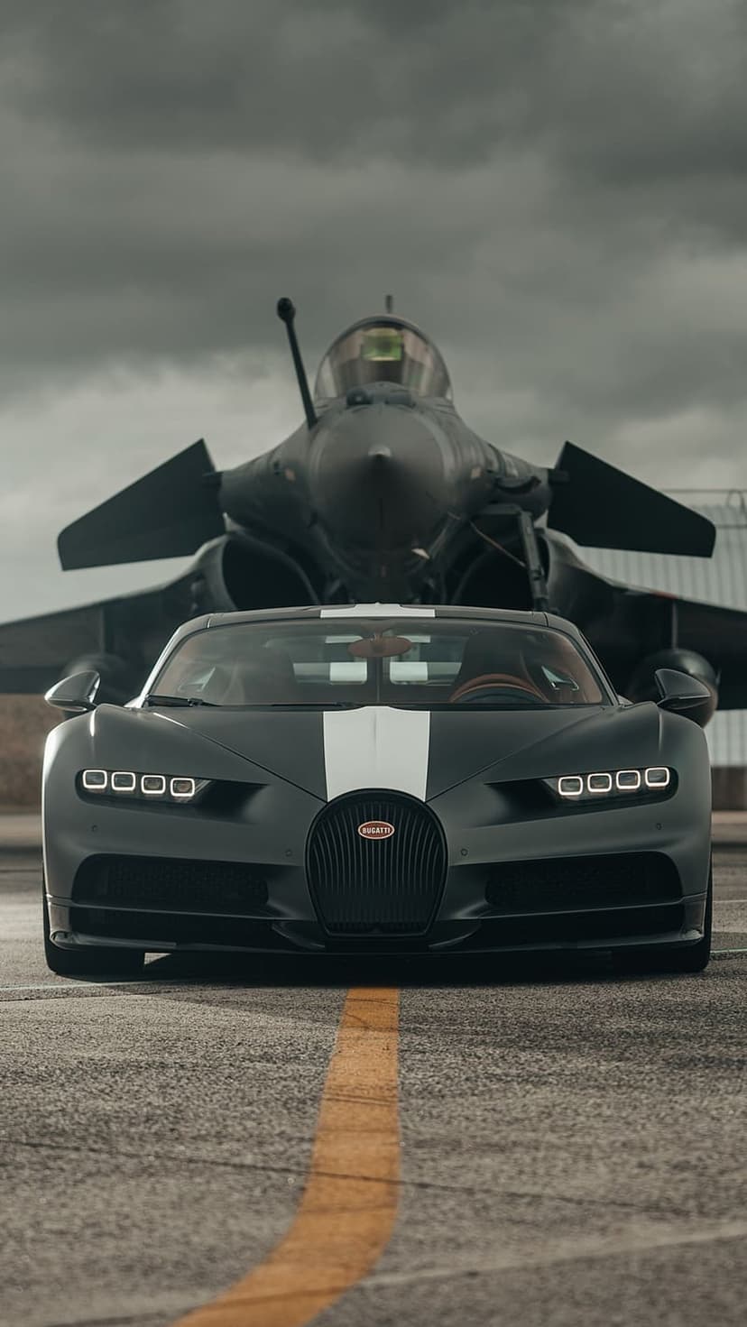 Bugatti Chiron hypercar in matte black parked on a tarmac runway in front of a grey military fighter jet at dusk.