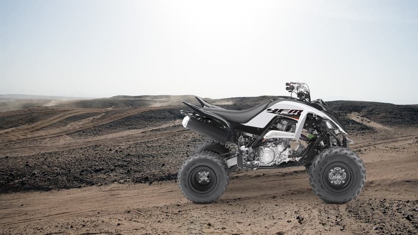 White Yamaha Raptor 700R quad bike on a dusty desert trail under a bright, hazy sky in landscape view.