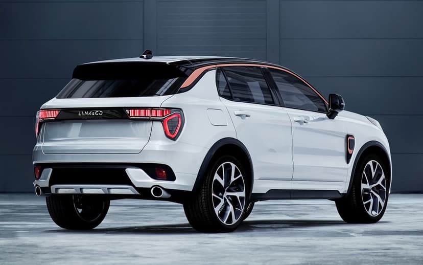 Rear view of a white Lynk & Co SUV with bronze accents parked against a dark grey industrial paneled wall.