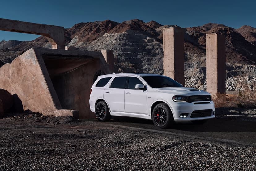 A white Dodge Durango SRT SUV parked among industrial concrete ruins with rocky desert mountains in the background.