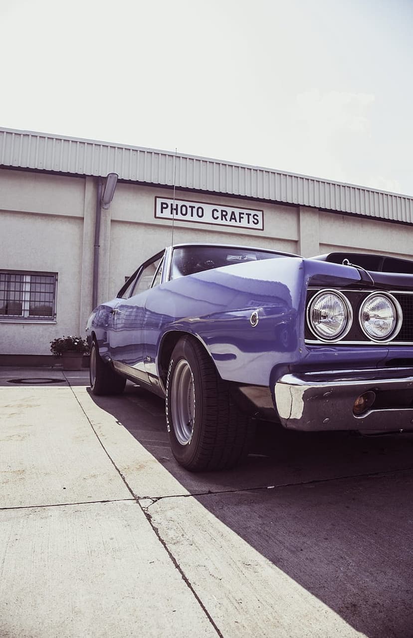 Purple 1968 Dodge Coronet muscle car with chrome bumpers parked on a concrete lot in front of a retro storefront.