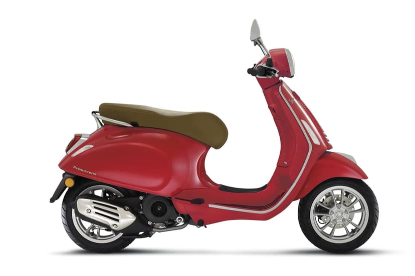 Red Vespa Primavera scooter featuring a brown saddle seat and silver chrome accents on a minimalist white background.
