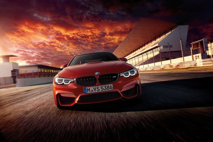Red BMW M4 driving on a race track at sunset with motion blur on the ground and dramatic orange clouds.