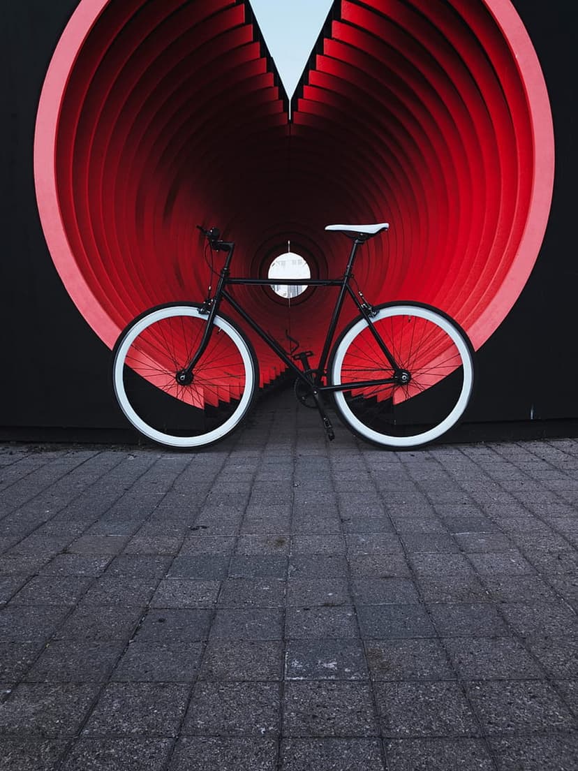 Black bicycle with white wheels positioned inside a red heart-shaped geometric tunnel installation.