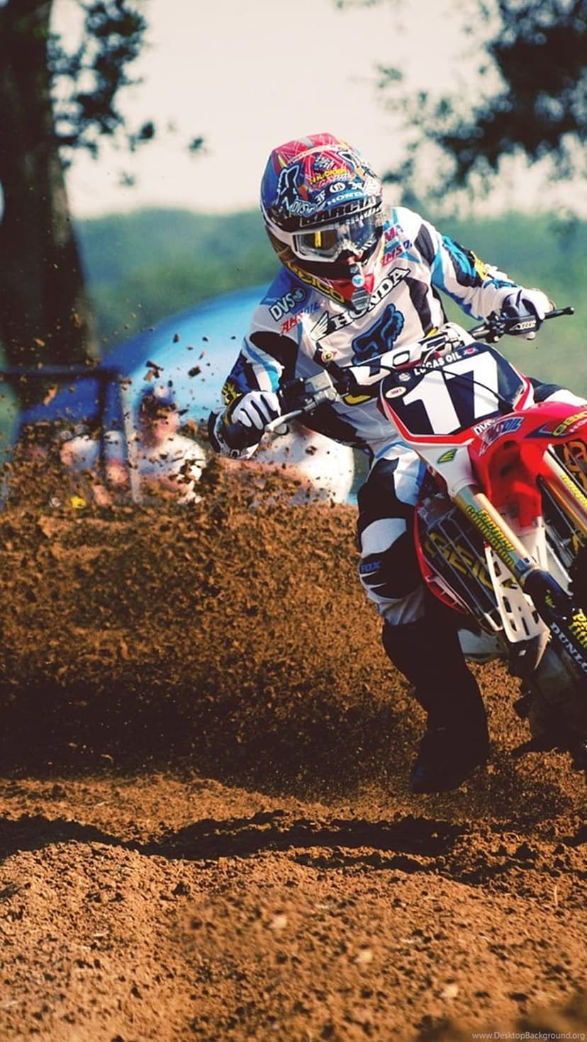 Motocross rider leans into a dirt track curve while spraying soil from a spinning rear motorcycle wheel.