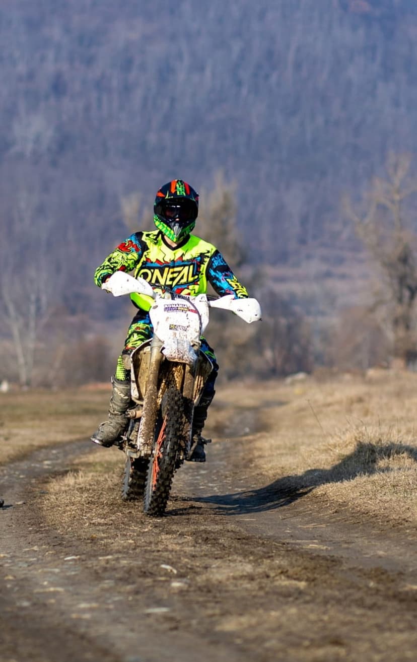 Motocross racer in protective gear leans into a turn on a dirt path, kicking up a thick trail of golden dust.