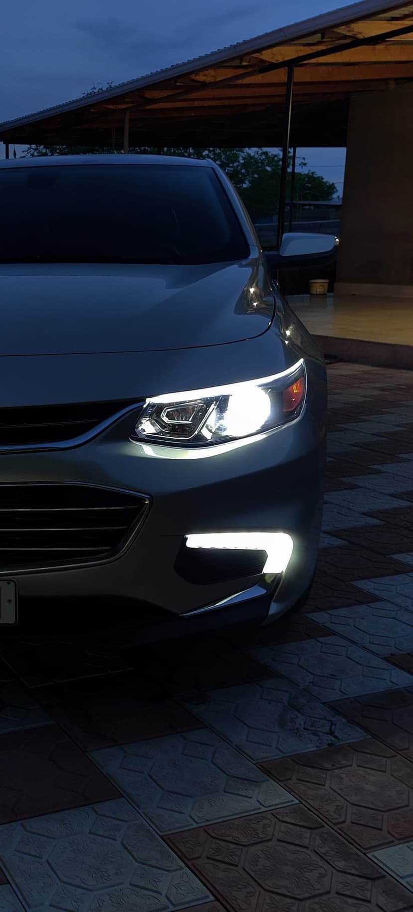 Modern car front view with bright LED headlights on a stone driveway during blue hour in a vertical orientation.