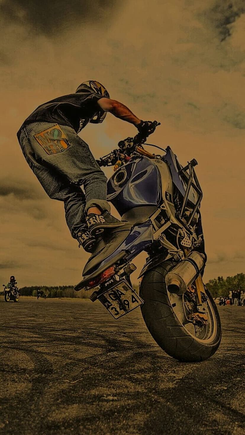 Motorcycle rider performing a vertical wheelie on a flat asphalt lot under a cloudy sky during an outdoor event.