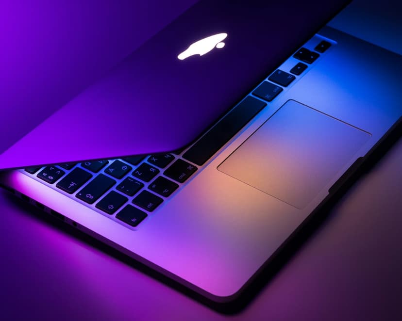 MacBook Pro keyboard and trackpad illuminated by deep purple light with a glowing white Apple logo on the lid.