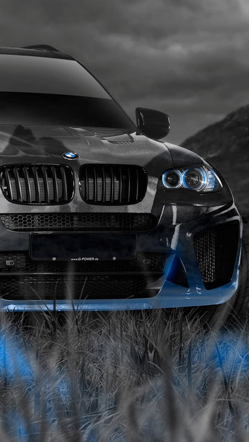 Black BMW X6 M with blue neon underglow parked in tall grass under a dark moody sky at a low camera angle.