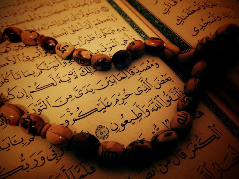 Open Quran with Arabic text beside a strand of wooden prayer beads under warm, focused lighting.