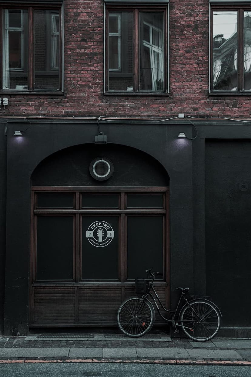 Vintage bicycle leans against a dark bar entrance below a red brick building during a moody urban evening.