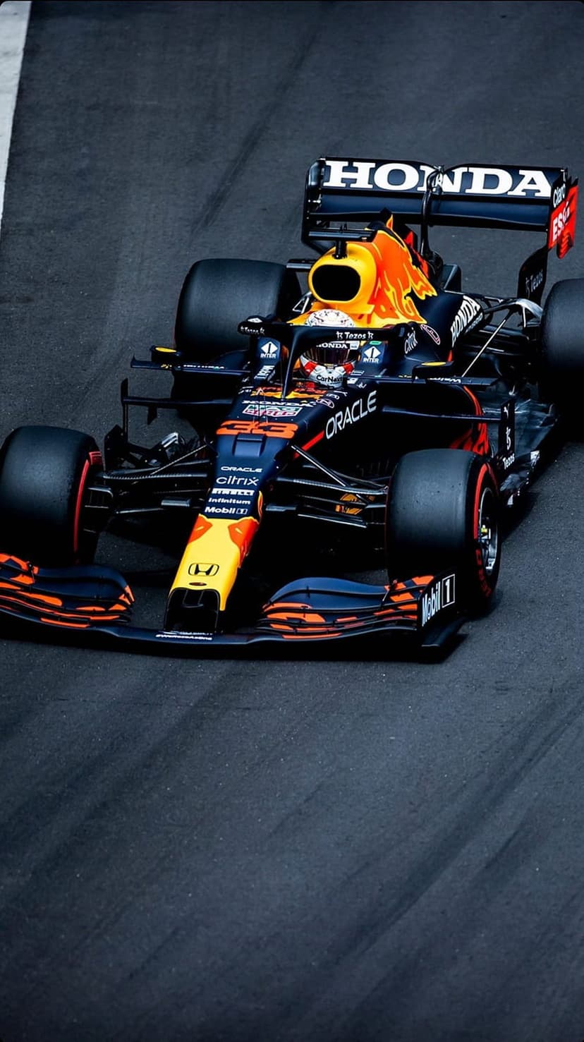 Red Bull Racing F1 car with Honda branding cruises at a low angle on a dark asphalt track during a race day.
