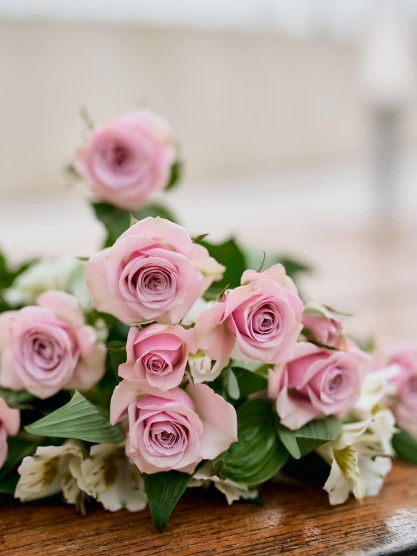 Soft pink roses and alstroemeria flowers lie on a dark wooden surface with a shallow depth of field effect.
