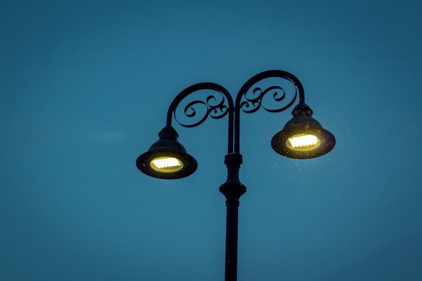 Double street lamp with ornate scrollwork silhouetted against a deep blue twilight sky with a warm amber glow.